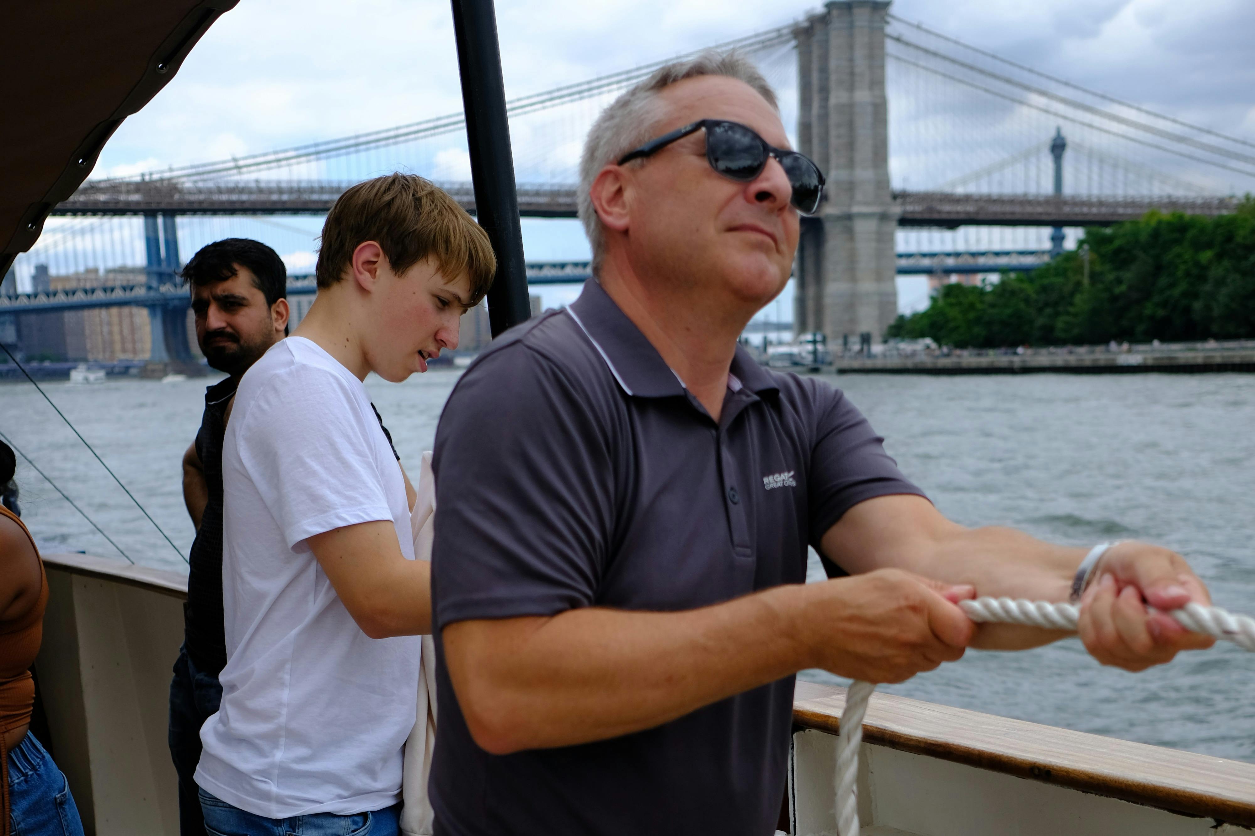 Guests helping to raise the sails with Brooklyn Bridge behind
