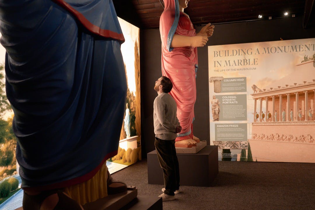 En person observerar en museiutställning med stora, färgglada statyer och en informationsutställning om fornminnen.