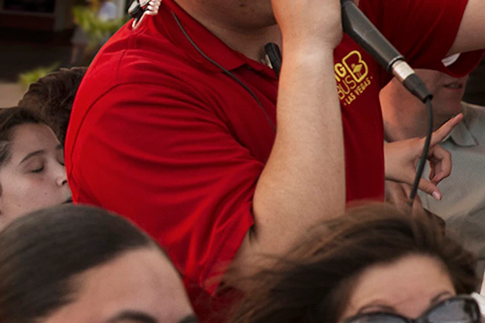 A tour guide speaks into a microphone, gesturing, while a group of excited passengers enjoy a sightseeing bus tour.
