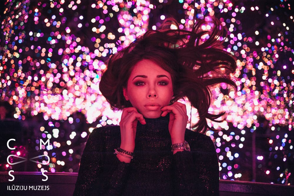 头发蓬乱的女士在色彩缤纷的散景灯前摆姿势，双手放在衣领上。