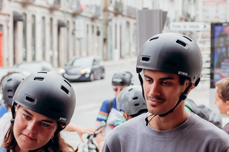 A group of people wearing helmets standing near bicycles, gathered in an urban outdoor setting.