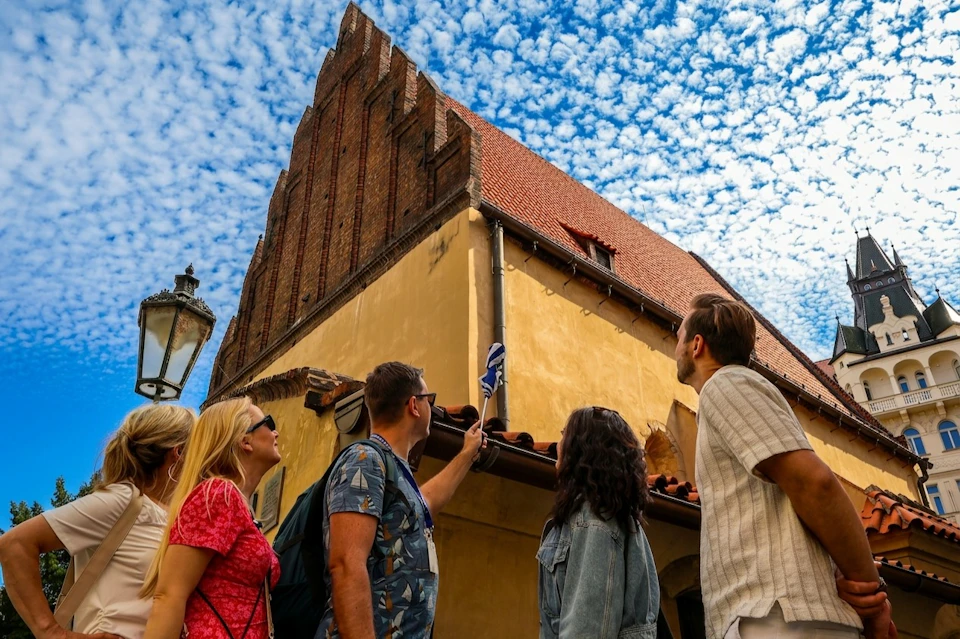 Four people stand near a historic building with steep, decorative gables under a sky filled with small, scattered clouds.