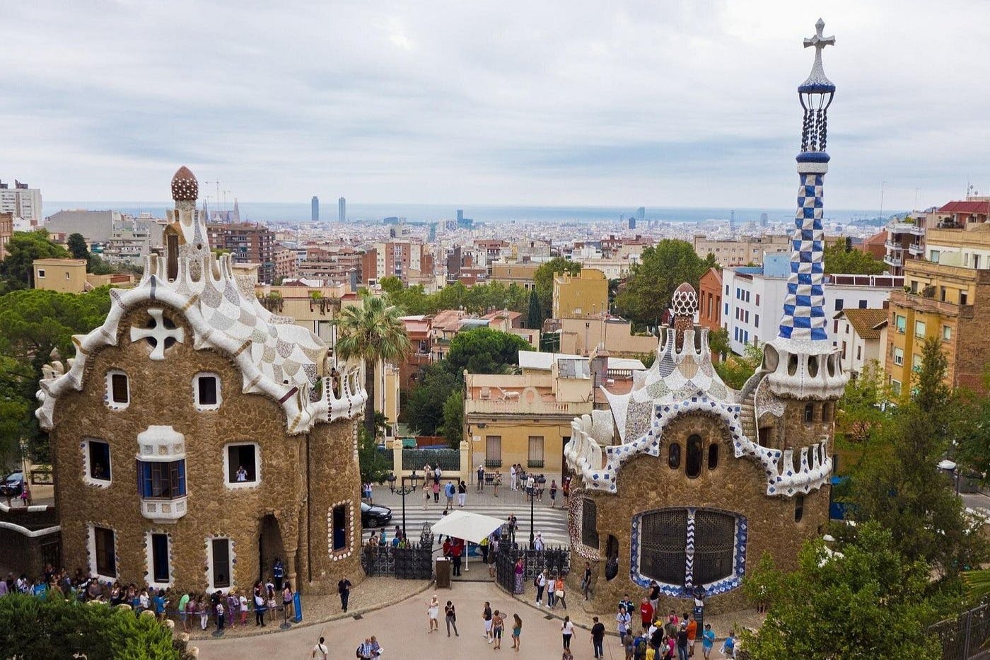 Vue du parc Güell à Barcelone, avec des structures architecturales colorées, des visiteurs et un paysage urbain en arrière-plan.