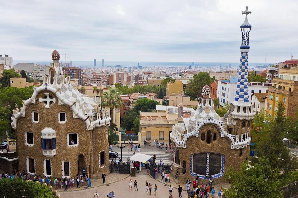 View of Park Güell in Barcelona, featuring colorful architectural structures, visitors, and a cityscape in the background.