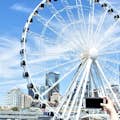 Seattle Great Wheel vom Wasser aus gesehen, mit einem Gast, der ein iPhone-Foto im Vordergrund macht.