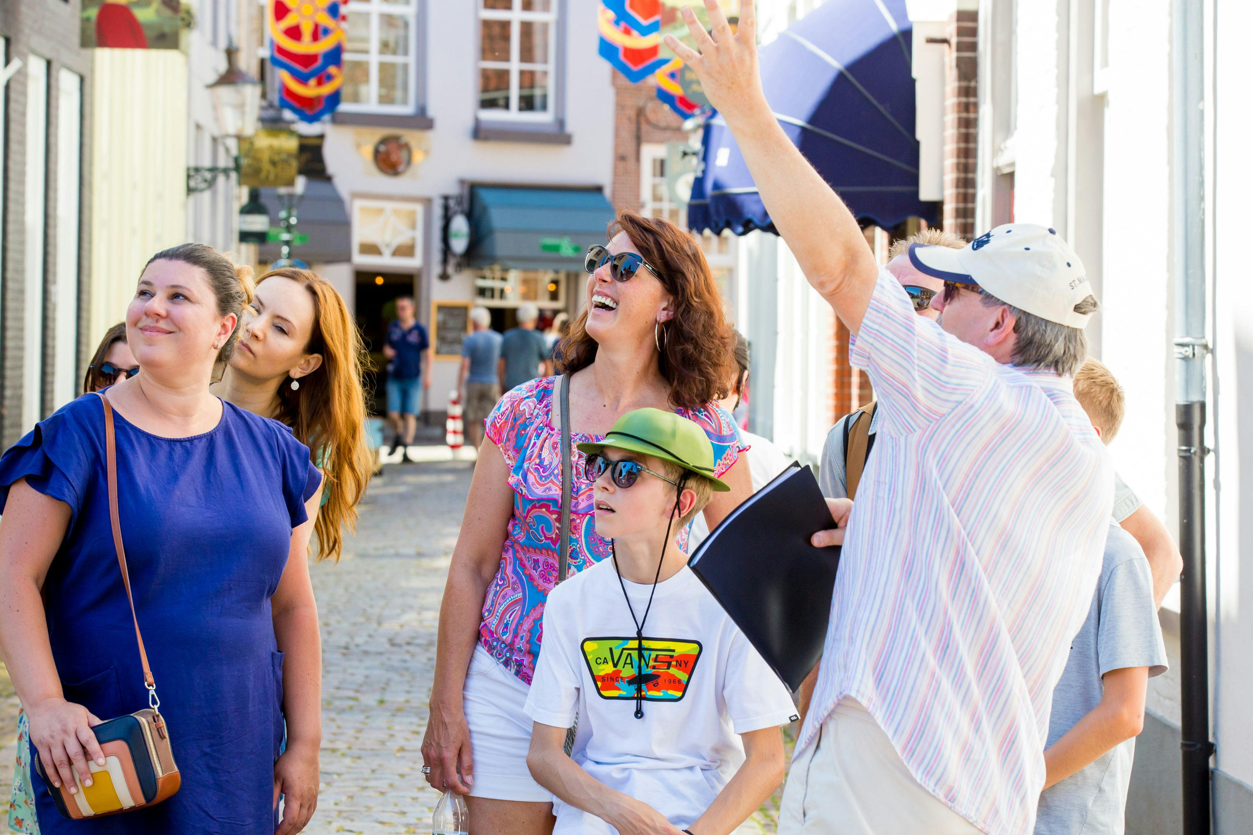 Un groupe de personnes souriantes et regardant vers le haut, peut-être en visite, dans une rue animée avec des bâtiments colorés et des décorations suspendues.