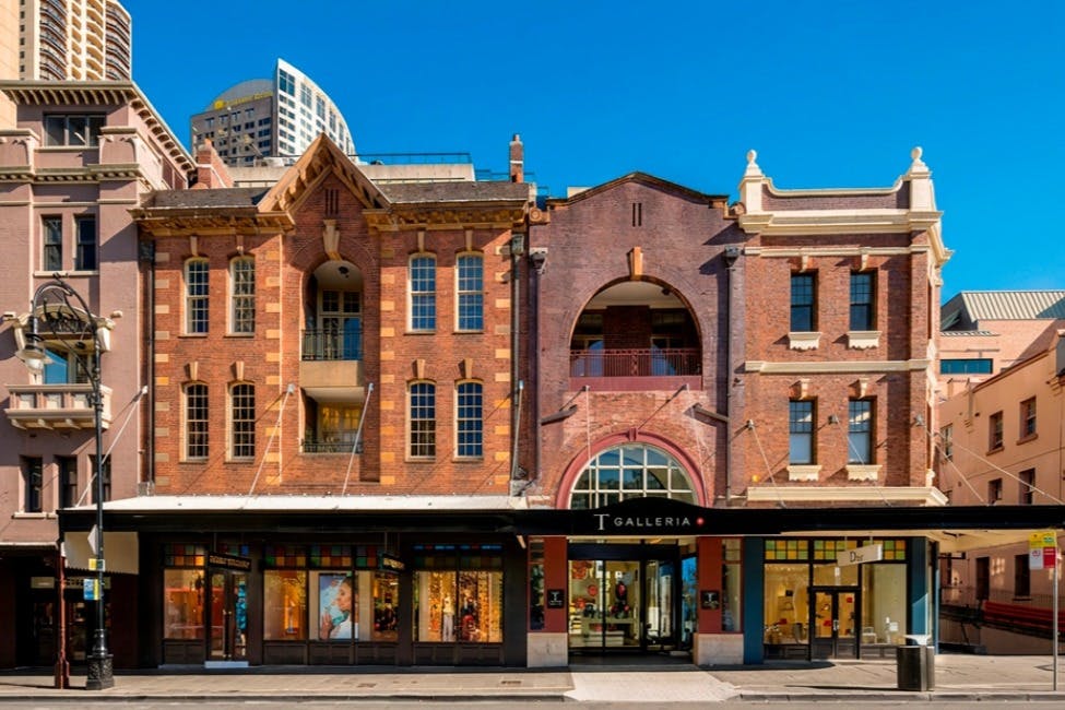 Um edifício histórico de tijolo vermelho que alberga a loja T Galleria, com grandes janelas e um céu azul ao fundo.