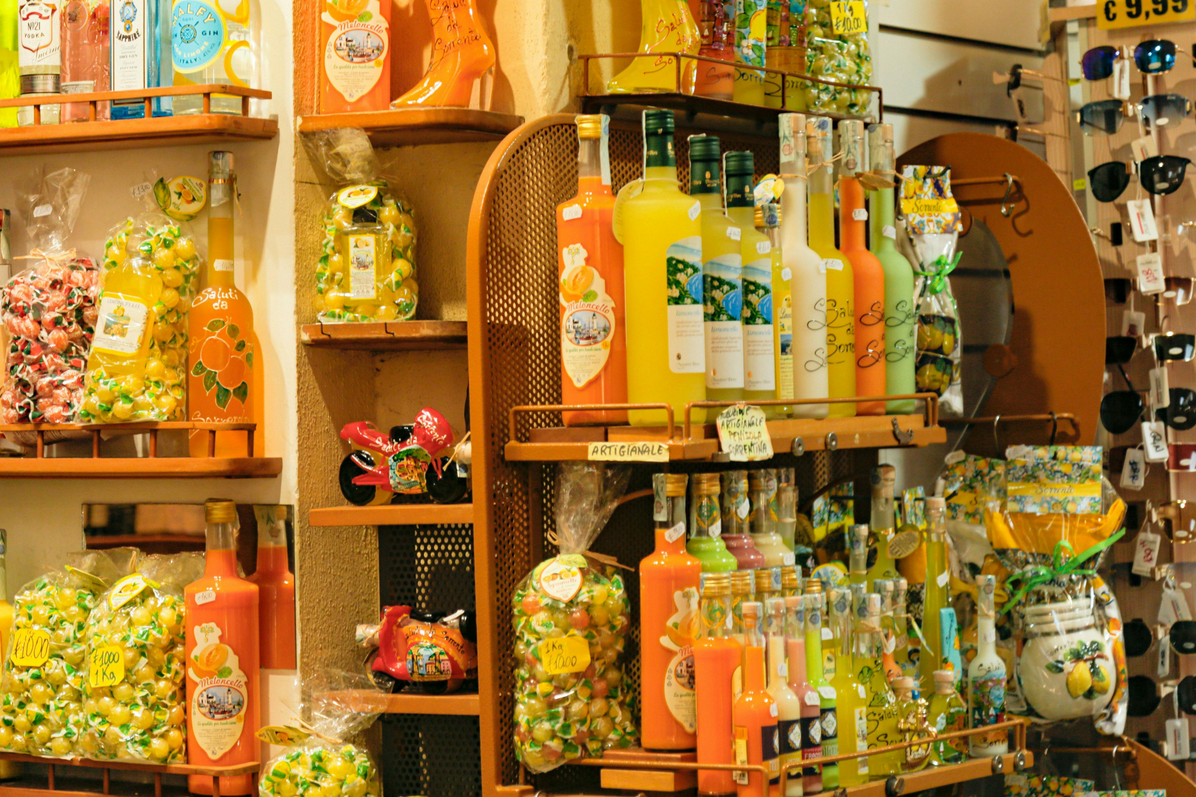 Schappen vol kleurrijke flessen met verschillende likeuren, zakken snoep en andere verpakte goederen in een winkel.