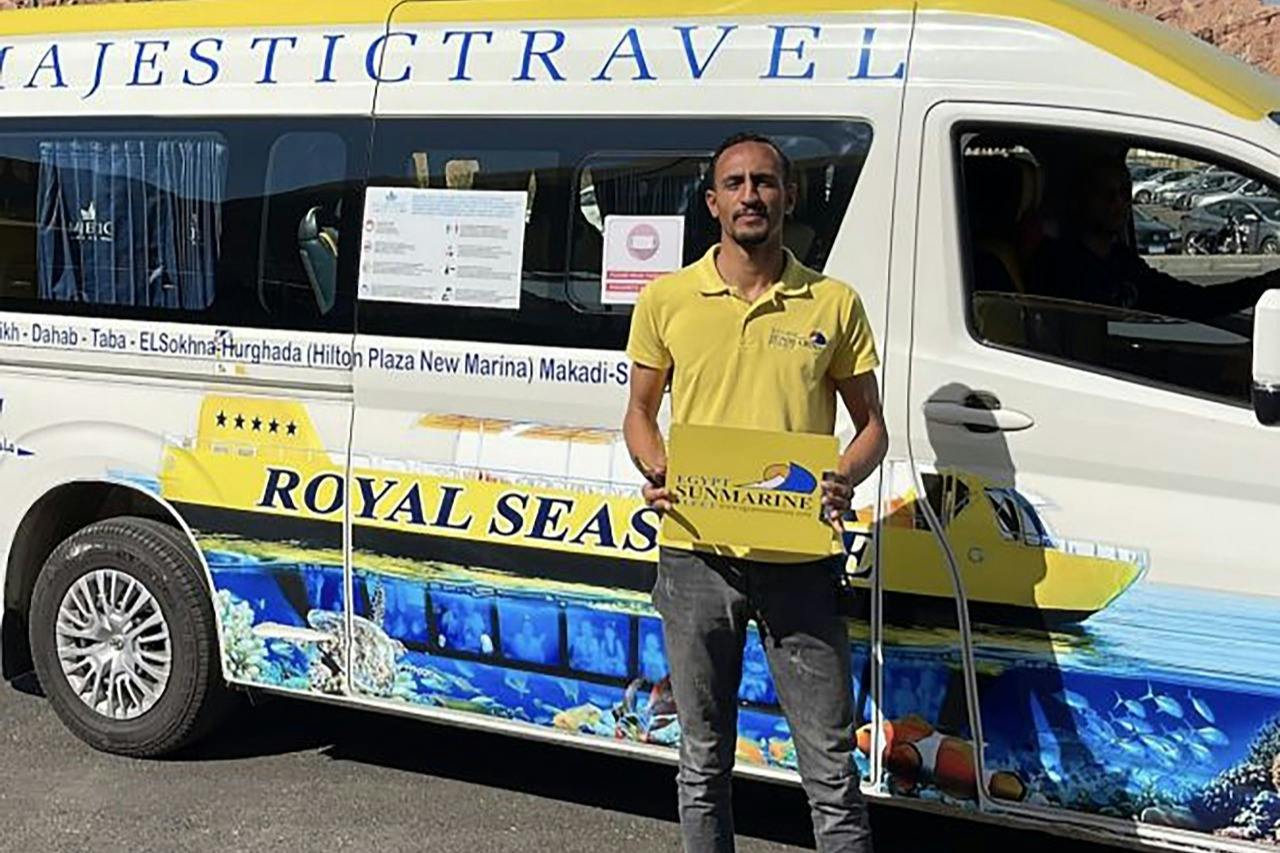 A man in a yellow shirt holds a sign reading 'Royal Sea Scope Submarine' in front of a van with ocean-themed design.
