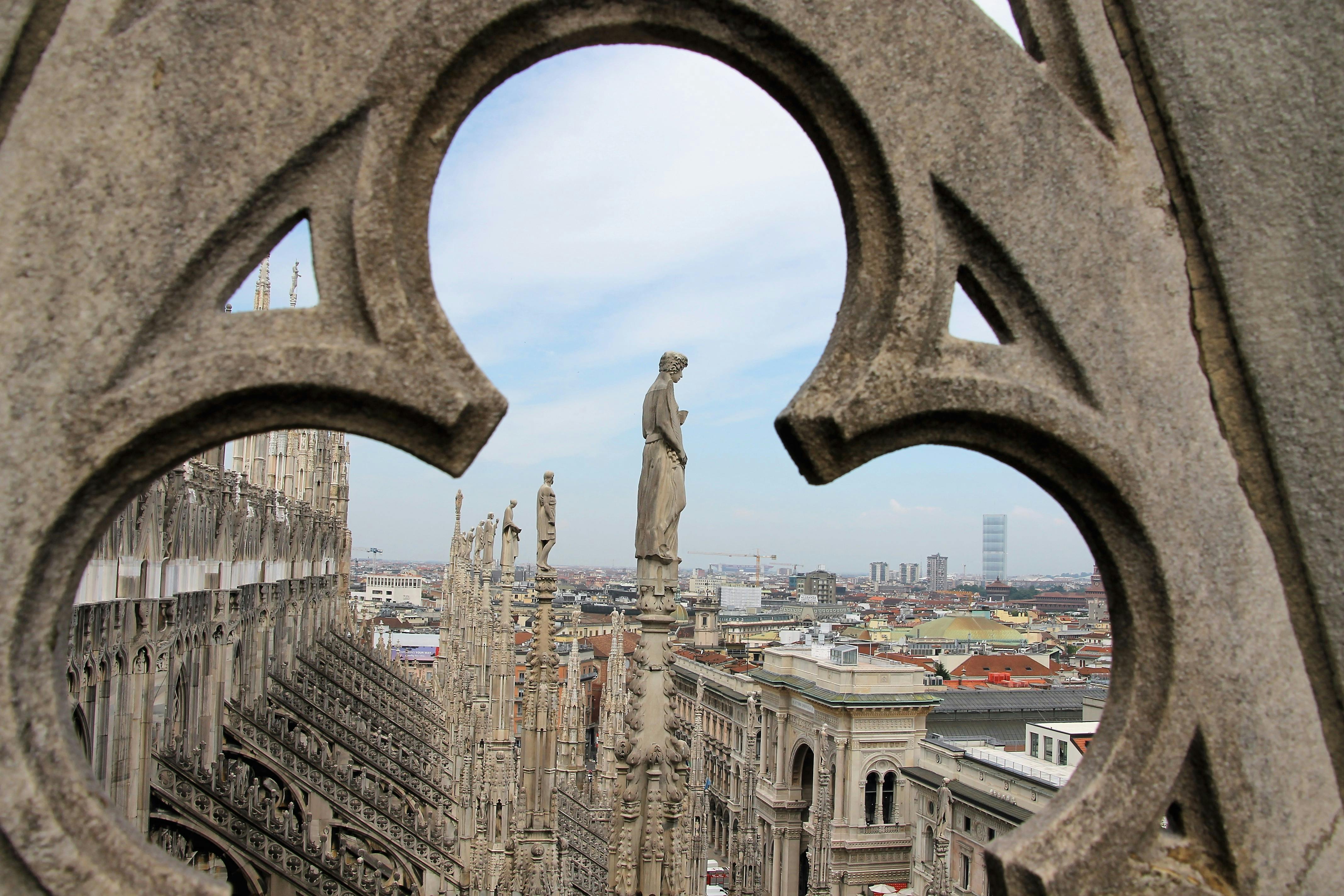 Aerial view of a city seen through an ornate stone frame, with statues atop a Gothic cathedral in the foreground.