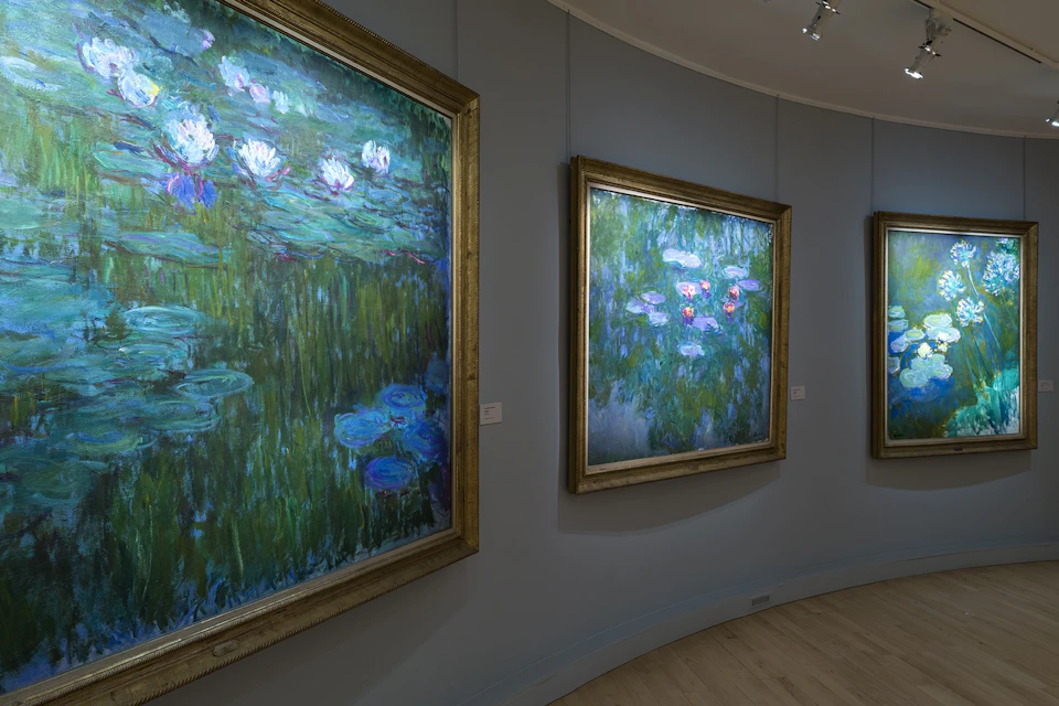 An art gallery displaying paintings of water lilies in ornate frames, mounted on a curved gray wall.