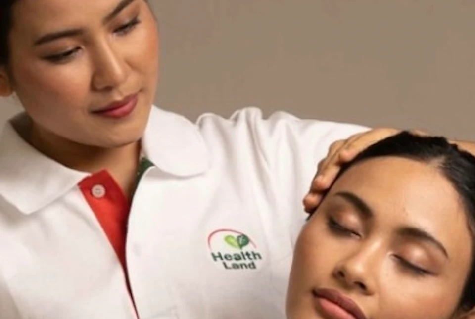A seated person receives a head and neck massage from another person standing behind them in a calm, neutral setting.