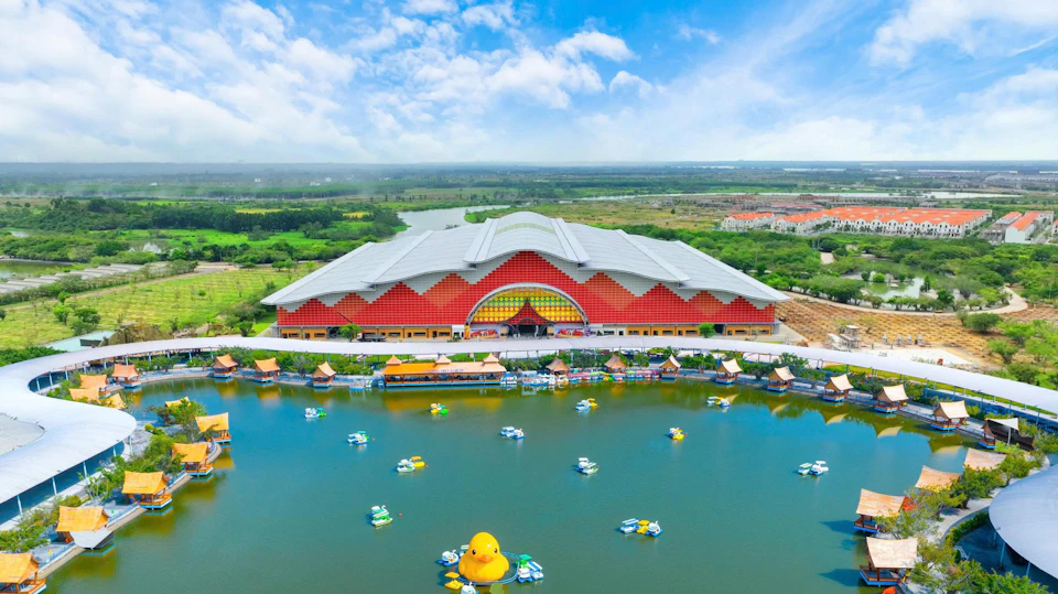 A large red and gray building with a decorative facade, located by a pond with floating structures and a large yellow duck.