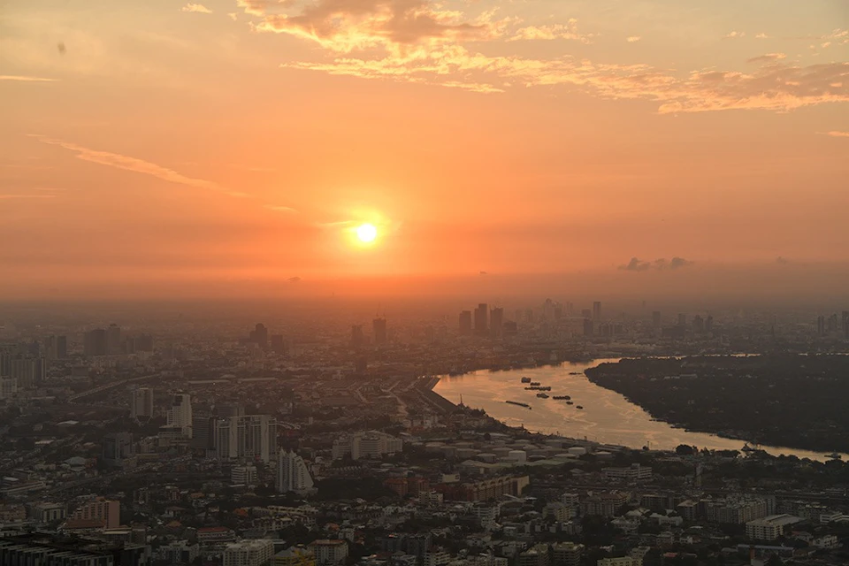 Cityscape at sunset with an orange sky, visible river, and scattered buildings and structures below.
