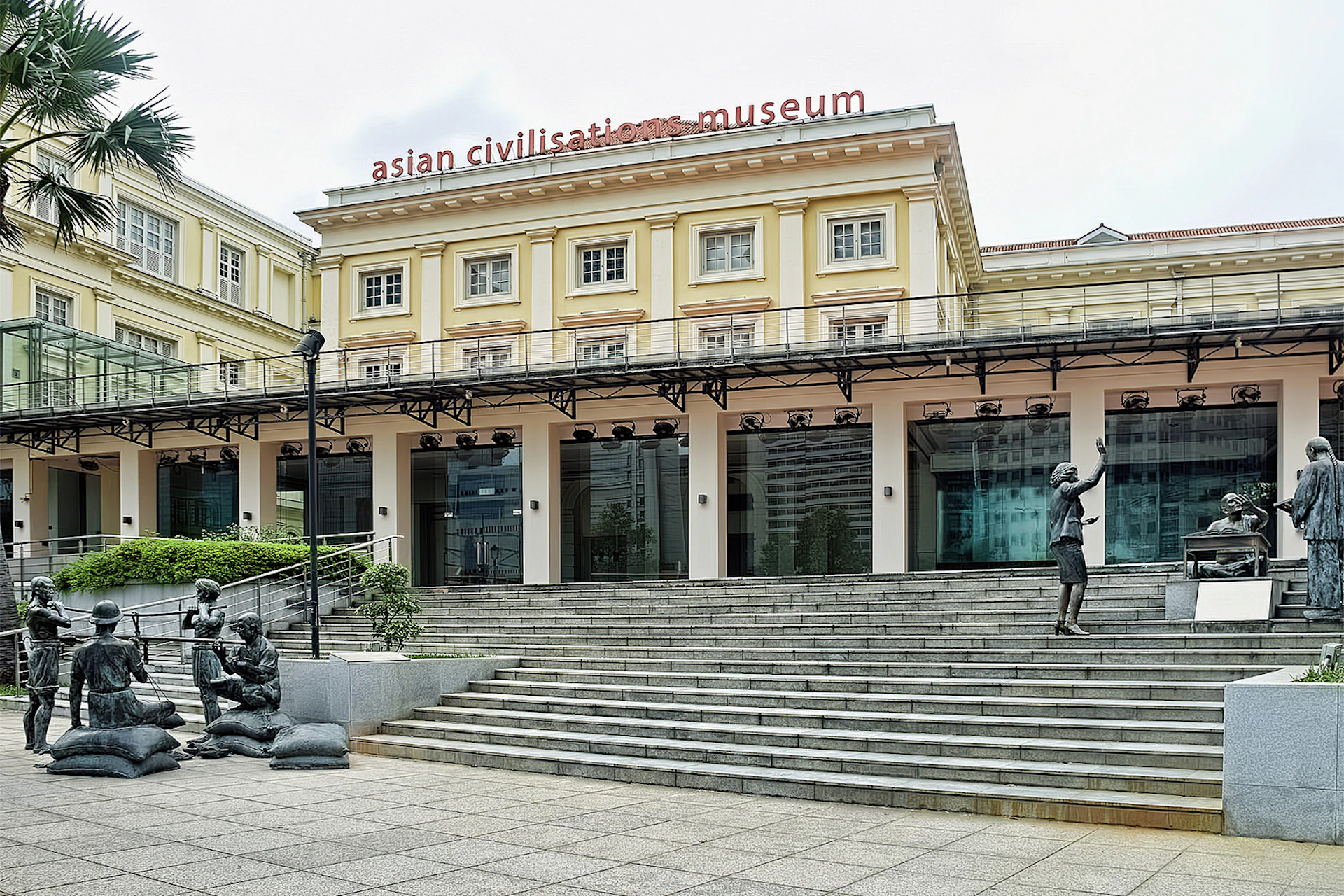 The Asian Civilisations Museum with a grand staircase, sculptures, and a beige facade under a partly cloudy sky.