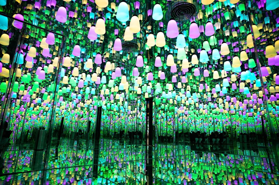 A mirrored room filled with colorful hanging lights in various shades of green, blue, purple, and yellow.