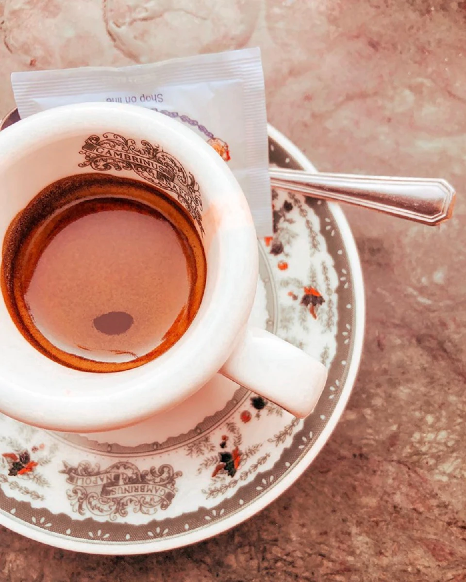 Espresso cup on a decorative saucer with a sugar packet and small spoon resting on the side.