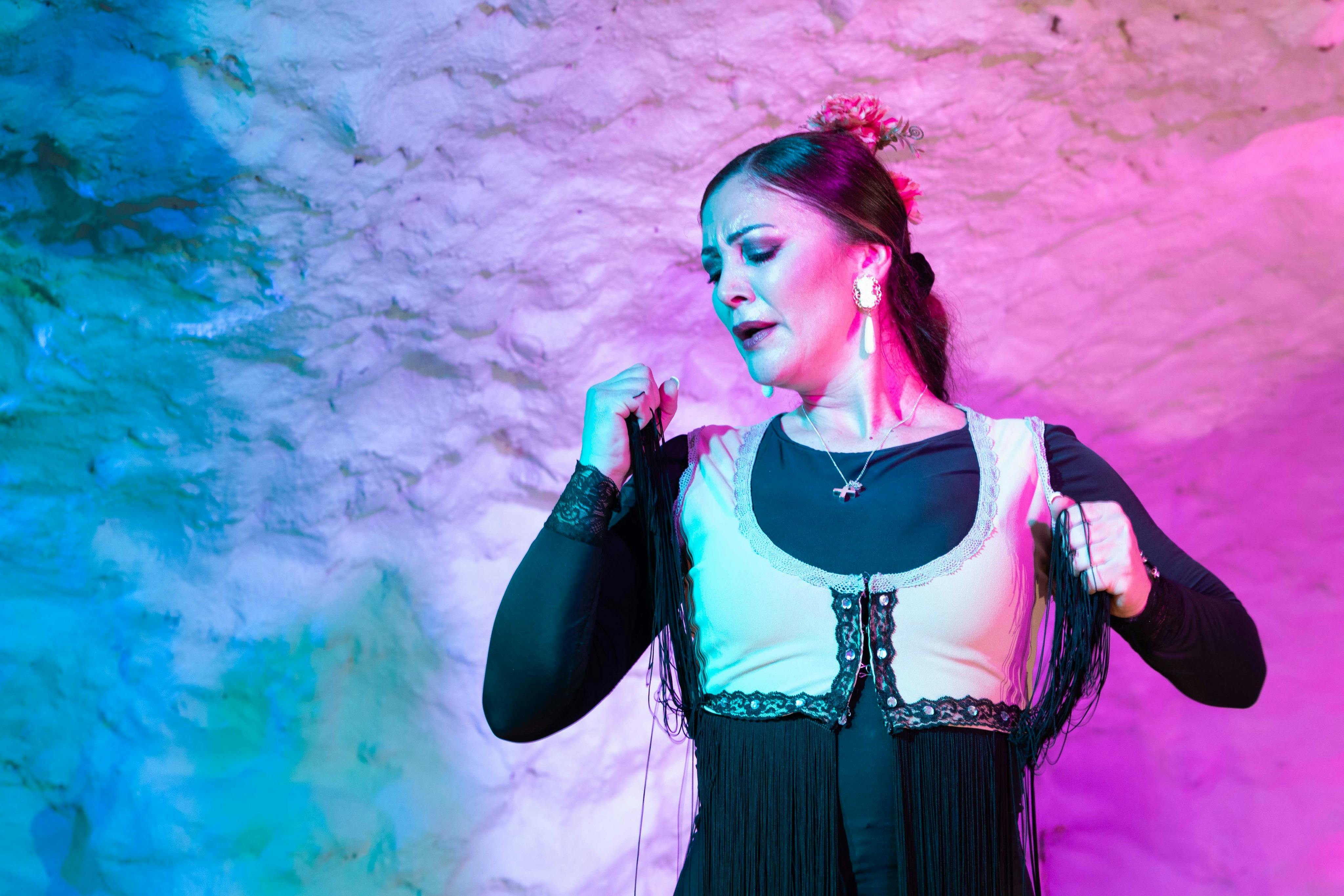 A woman performing a dance or expression, wearing traditional attire, against a textured, colorfully lit background.