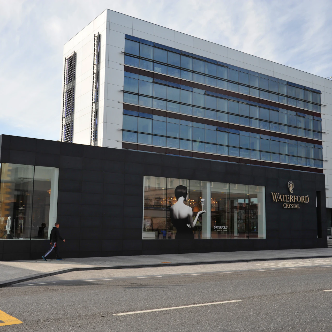 The image shows a modern building with a glass facade and signage for "Waterford Crystal." A few pedestrians are walking by.