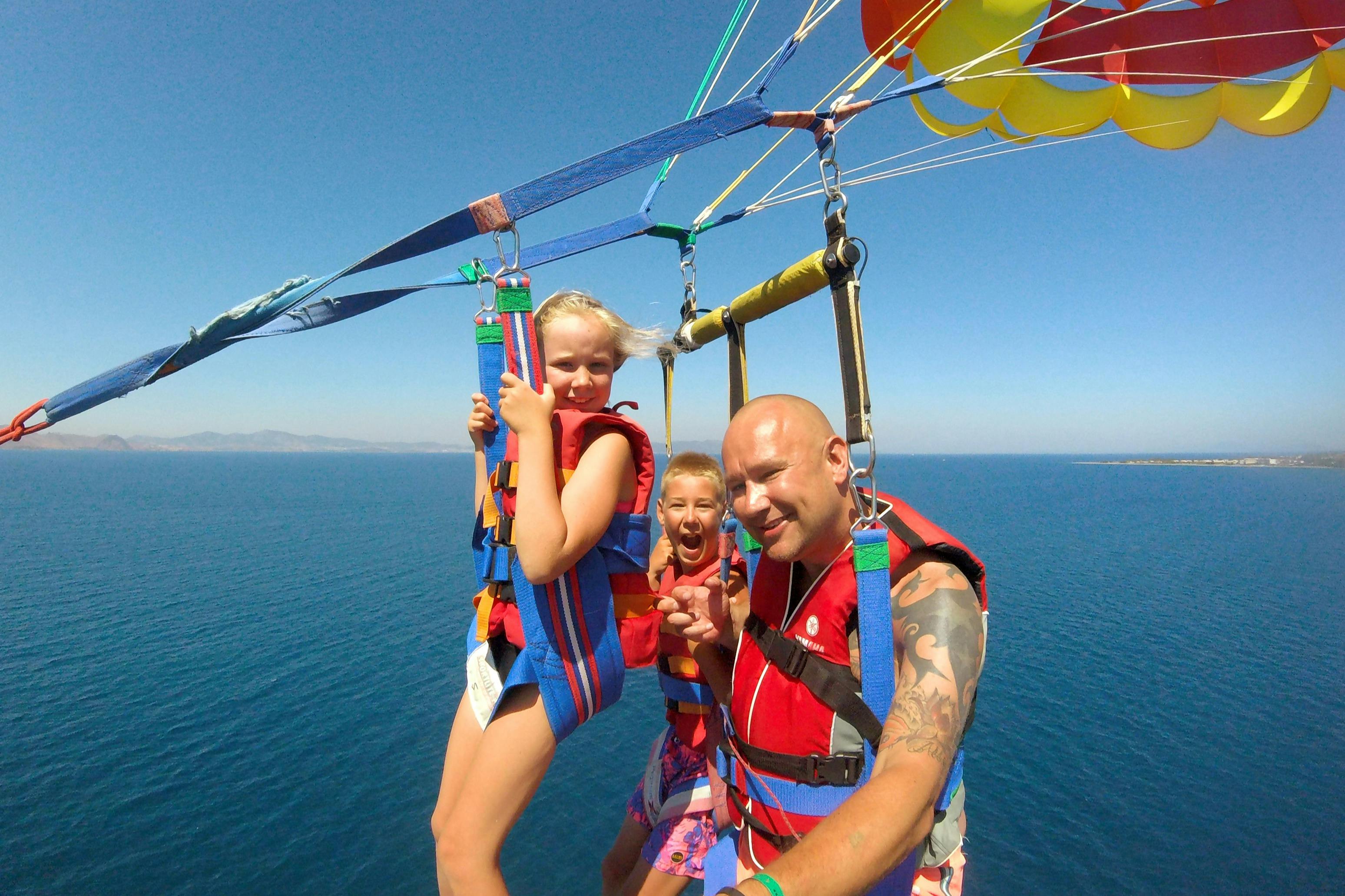 Three individuals wearing harnesses and life vests parasailing over the ocean on a clear, sunny day.