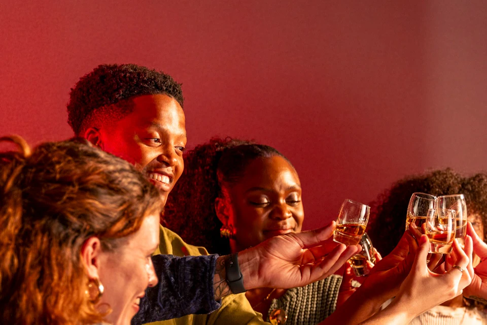 A group of people standing around a table, raising glasses in a celebratory toast under warm lighting.