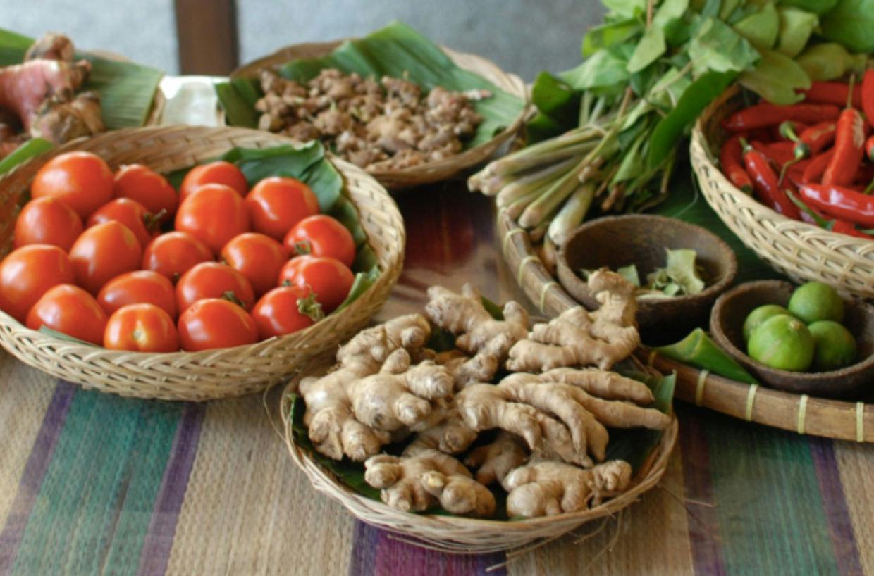Układ świeżych warzyw i ziół w tkanych koszykach, w tym pomidorów, imbiru, papryki chili i limonek.