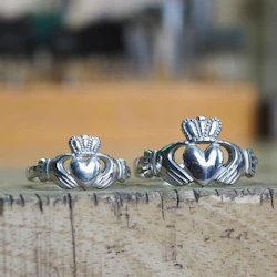 Two silver Claddagh rings with heart, crown, and hands designs displayed on a wooden surface.