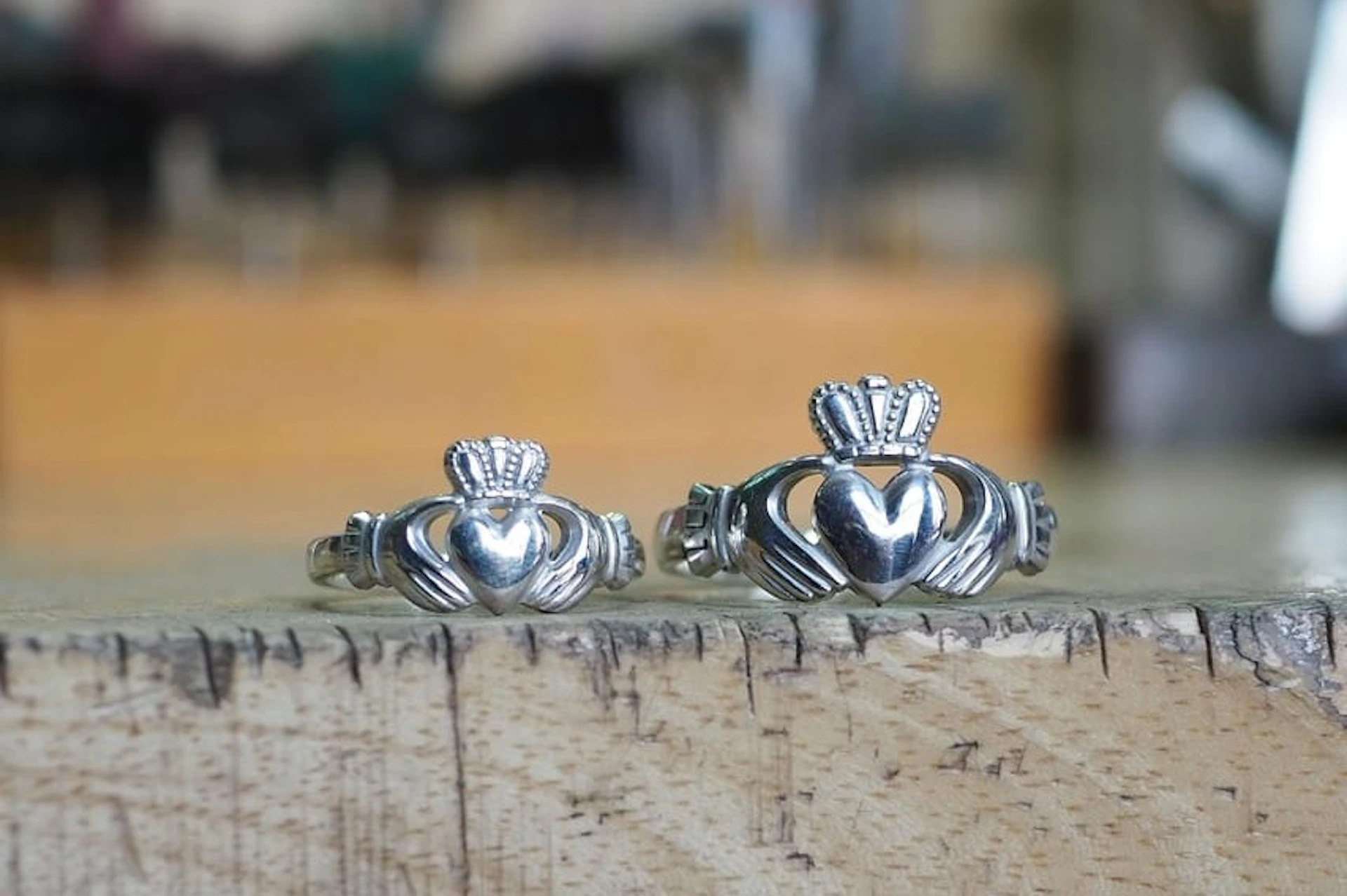 Two silver Claddagh rings with heart, crown, and hands designs displayed on a wooden surface.