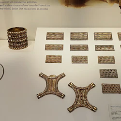 Visning av antika guldartefakter, inklusive armband, plaketter och dekorativa bitar, tillsammans med en informationspanel.