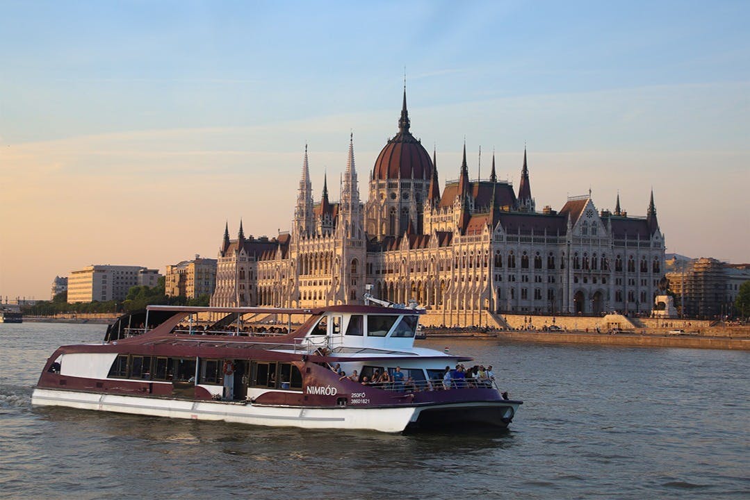 Ein Boot auf einem Fluss mit dem ungarischen Parlamentsgebäude im Hintergrund bei Sonnenuntergang.