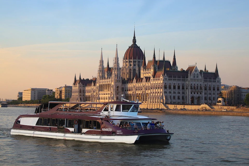 A boat on a river with the Hungarian Parliament Building in the background during sunset.