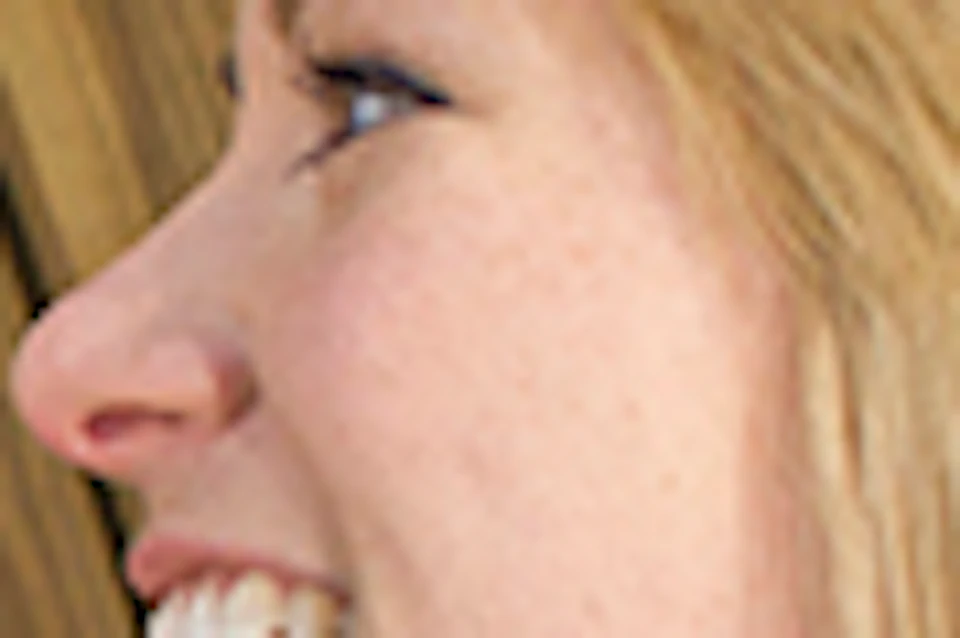 A woman with blonde hair and a purple shirt smiling as she places a small object into a crack in a wooden wall.