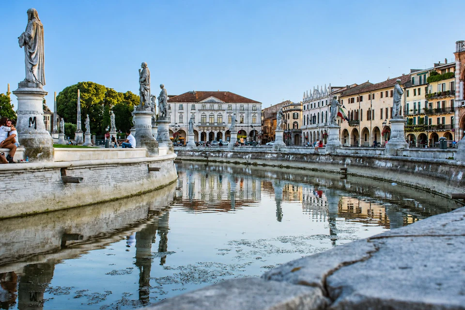 A scenic view of a canal lined with statues and historic buildings under a clear blue sky.