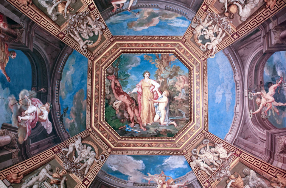 Ornate ceiling fresco depicting mythological figures, surrounded by intricate architectural detailing and vibrant blue sky background.