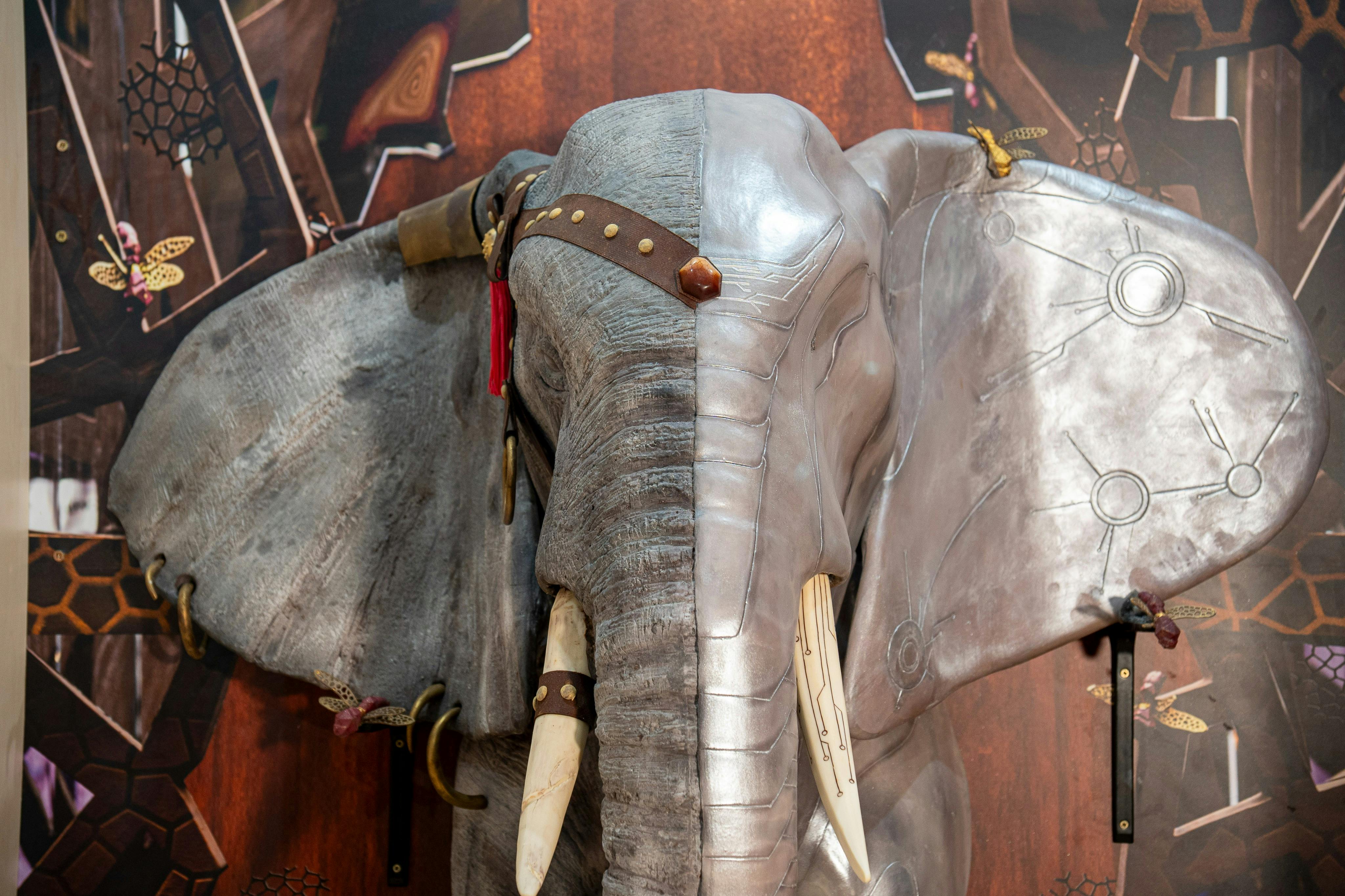 Une présentation sculpturale d'une tête d'éléphant dont une moitié est métallique et l'autre texturée, avec des défenses et des lanières.
