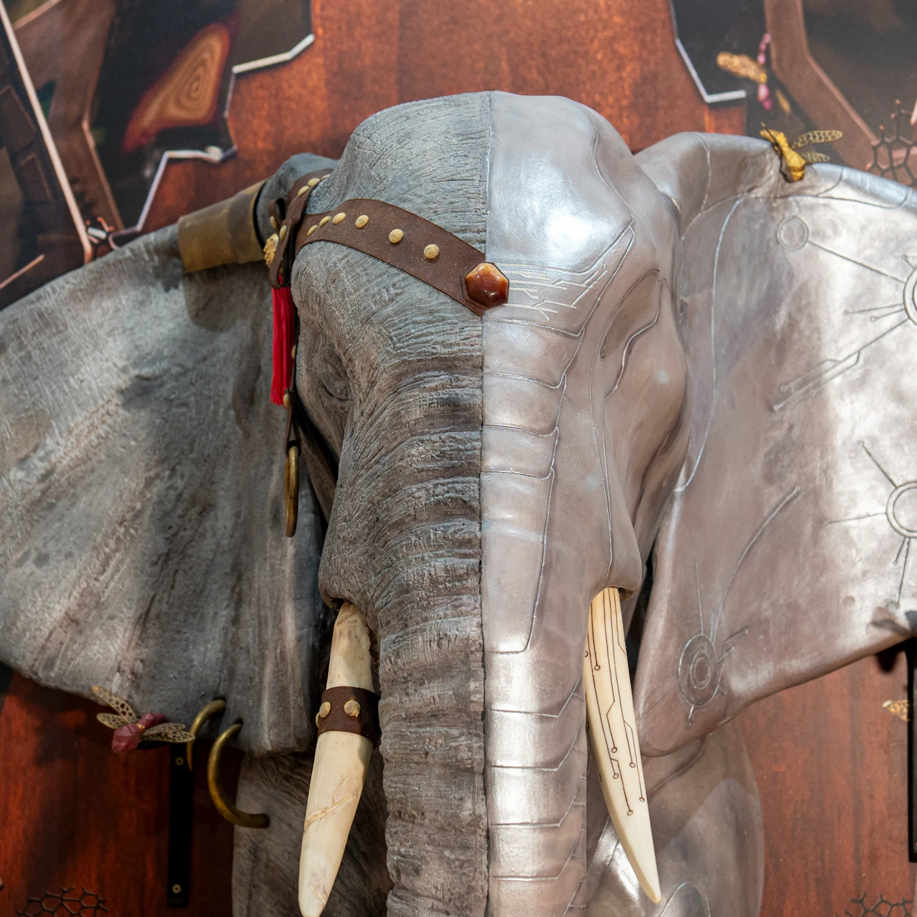 A sculptural display of an elephant's head with one half metallic and the other textured, featuring tusks and straps.