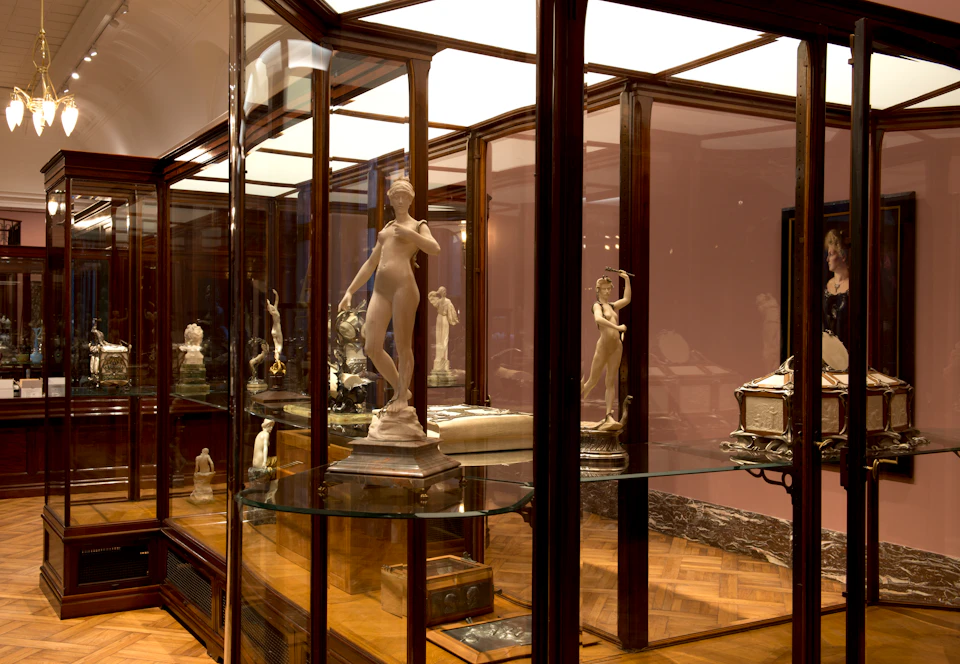 A museum display of glass cabinets showcasing several classical-style marble statues.