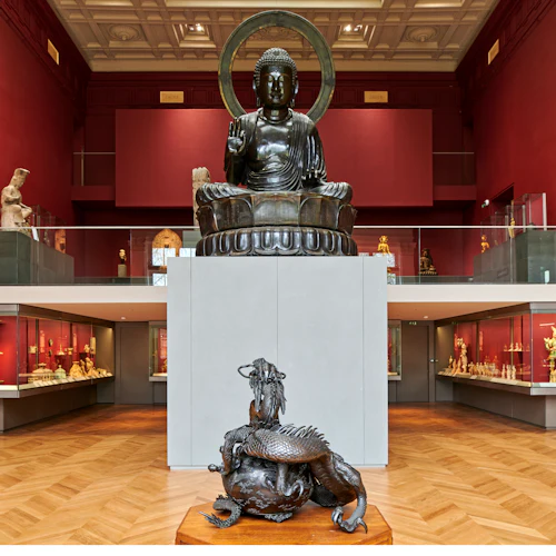 Ett museum med en stor Buddha-staty, utställningsväskor med artefakter och en drakskulptur i förgrunden.