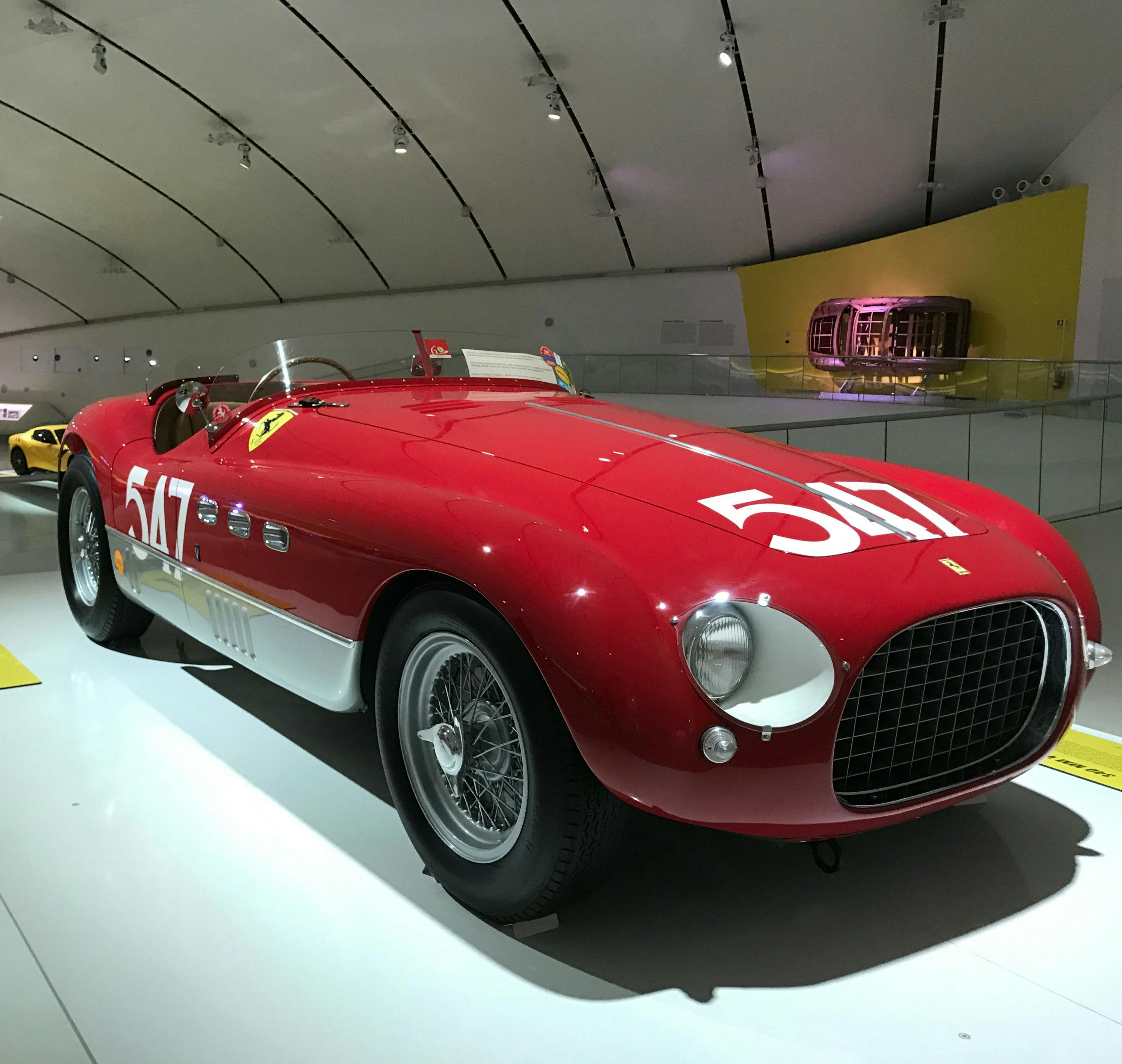 Voiture de course rouge de collection portant le numéro 517 sur le capot et les flancs, exposée dans une salle d'exposition bien éclairée au plafond incurvé.