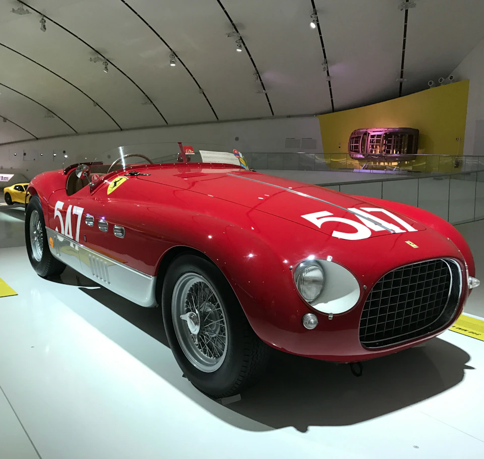 Red vintage race car with the number 517 on its hood and sides, displayed in a well-lit showroom with a curved ceiling.