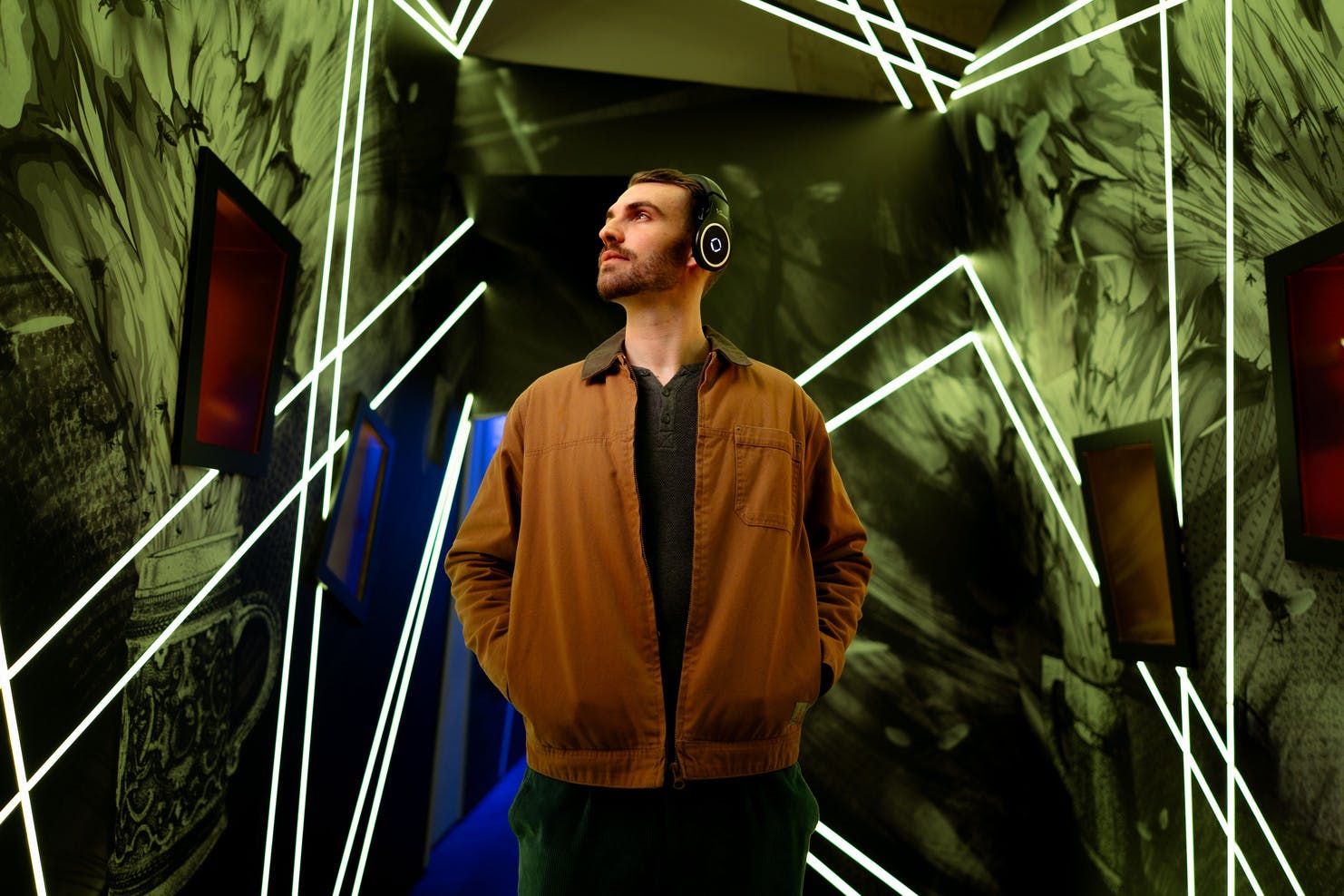 一个戴着耳机的人站在现代化的走廊里，走廊上有发光的几何线条和抽象的墙壁图案。