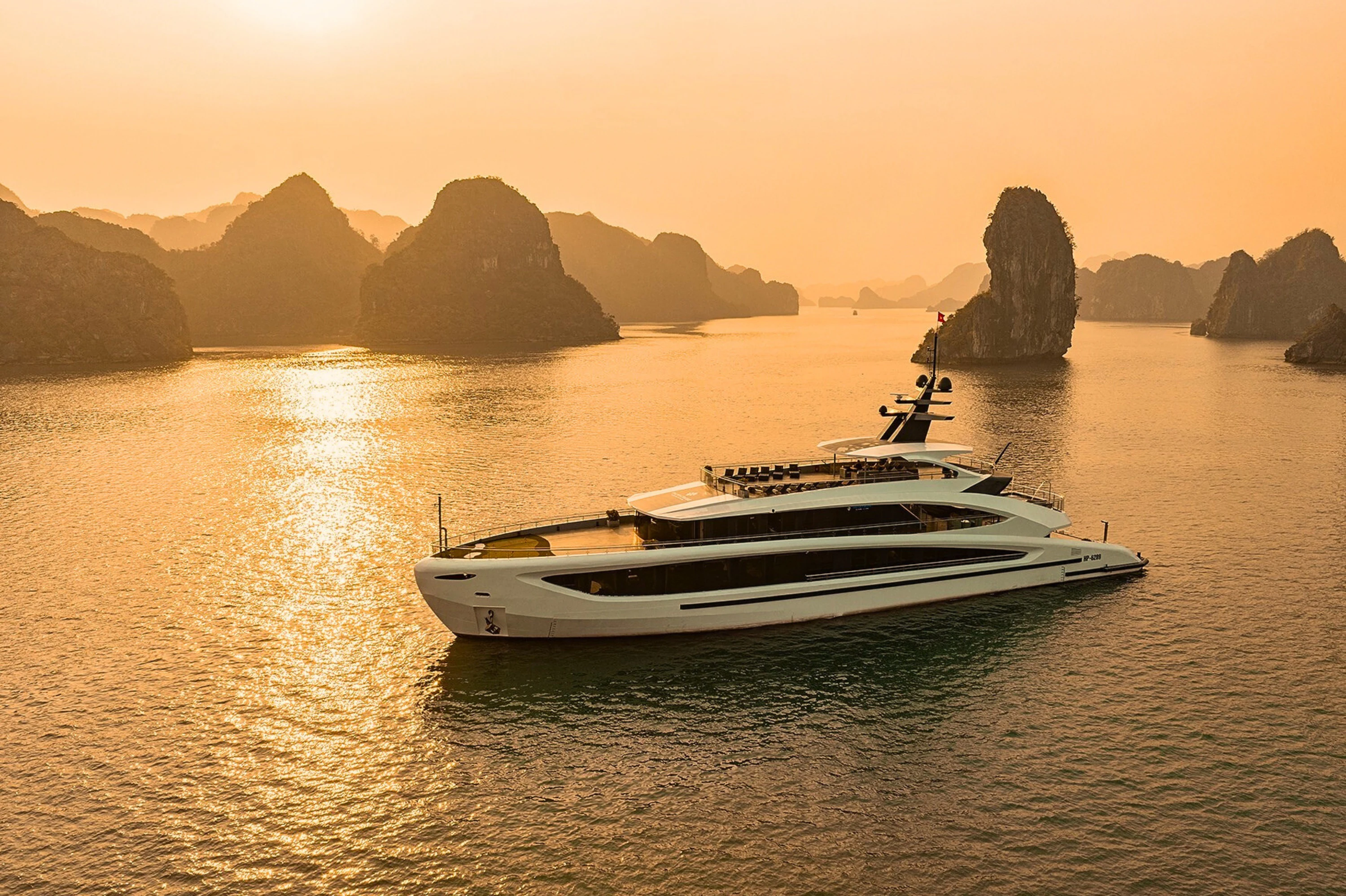 A white yacht on calm water during sunset, surrounded by tall, rocky islands.