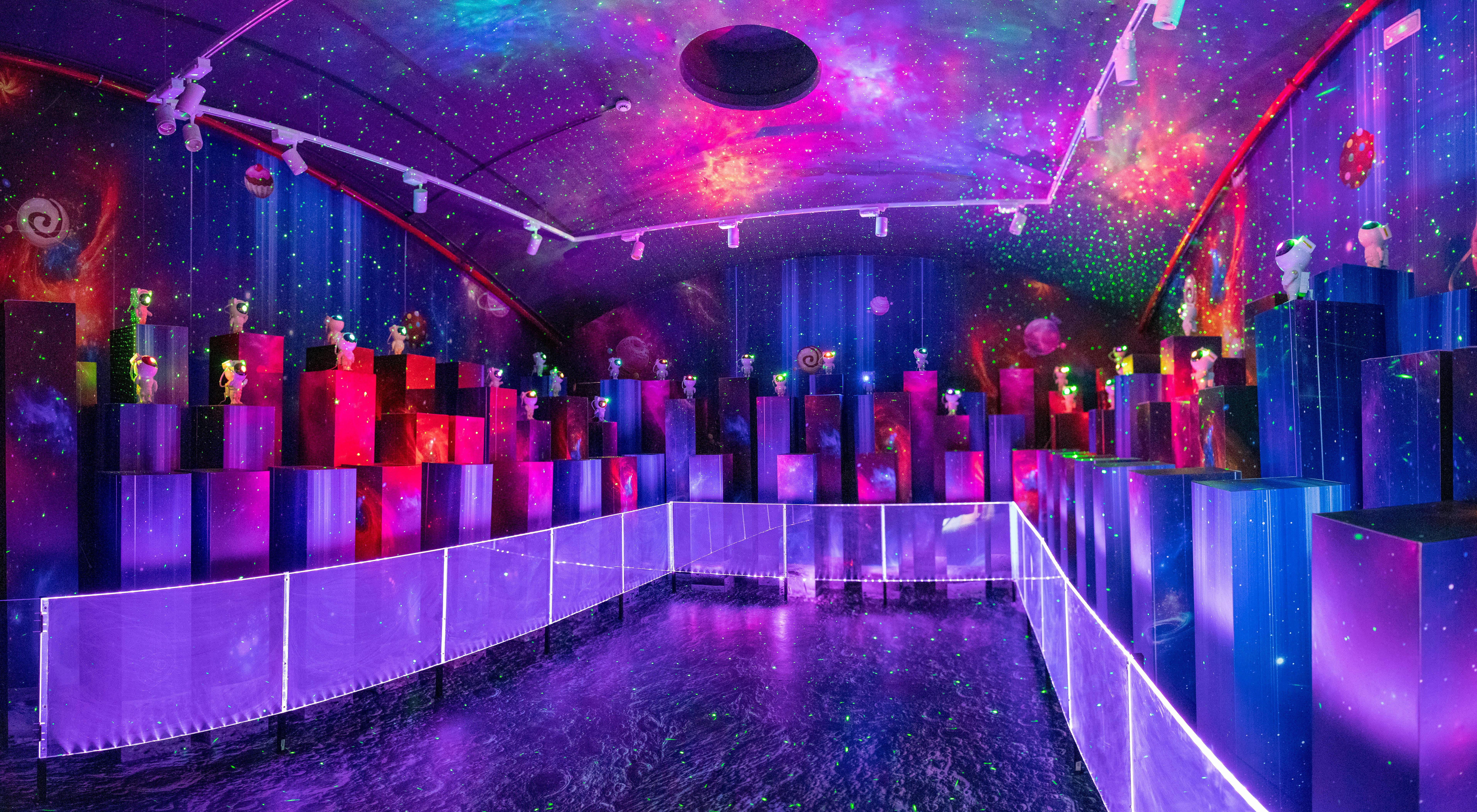 A room with a cosmic-themed decor, featuring glowing purple and pink lights, reflective surfaces, and numerous colorful structures.