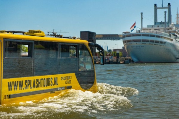 "SPLASHTOURS" 라고 표시된 노란색 수륙양용 버스가 대형 선박을 배경으로 물 위에 정박해 있습니다.