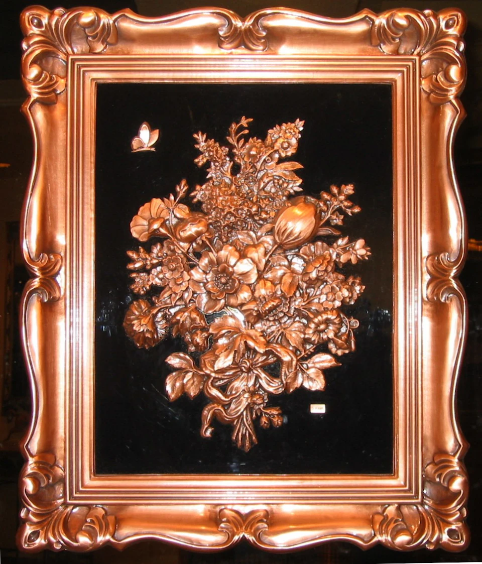 Ornate wooden frame with a copper-colored floral relief and a small butterfly on a black background.