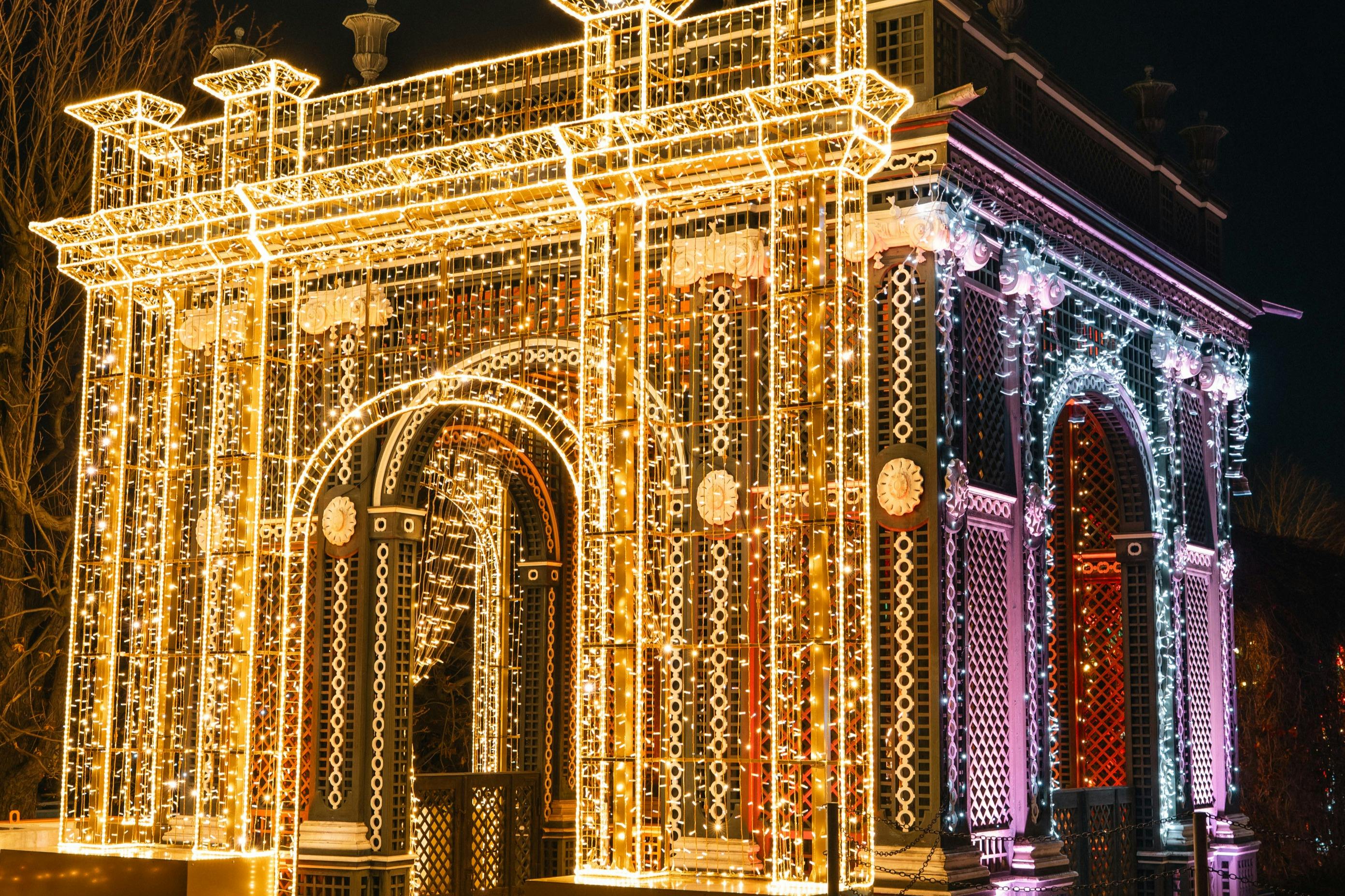 En udsmykket struktur dækket af indviklede gyldne og hvide lys, oplyst om natten, med buer og dekorative detaljer.