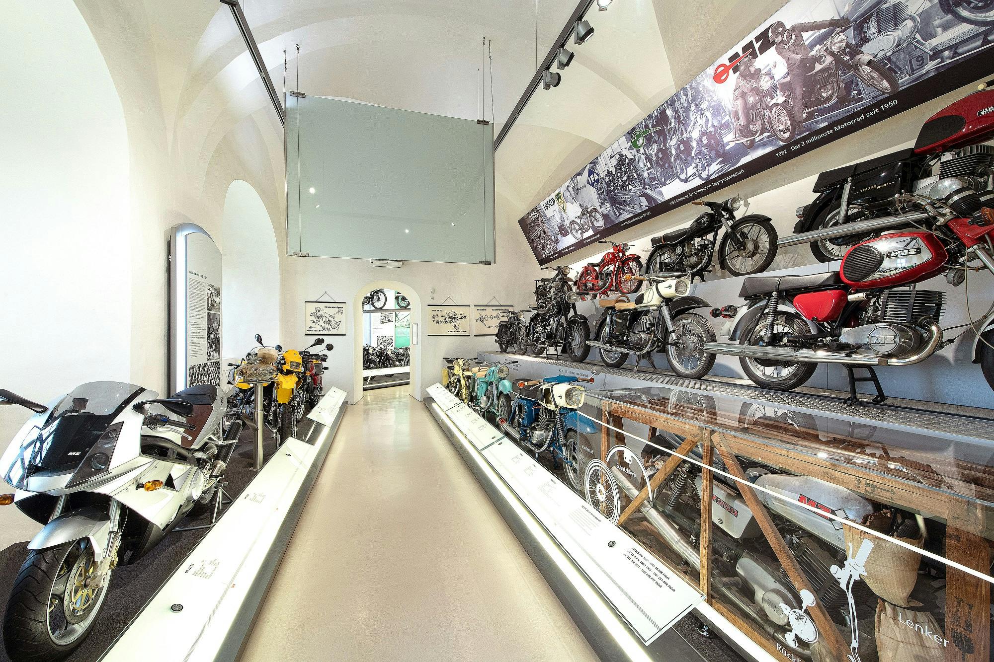 博物馆展览展示了老式摩托车，墙上挂着信息牌和历史照片。