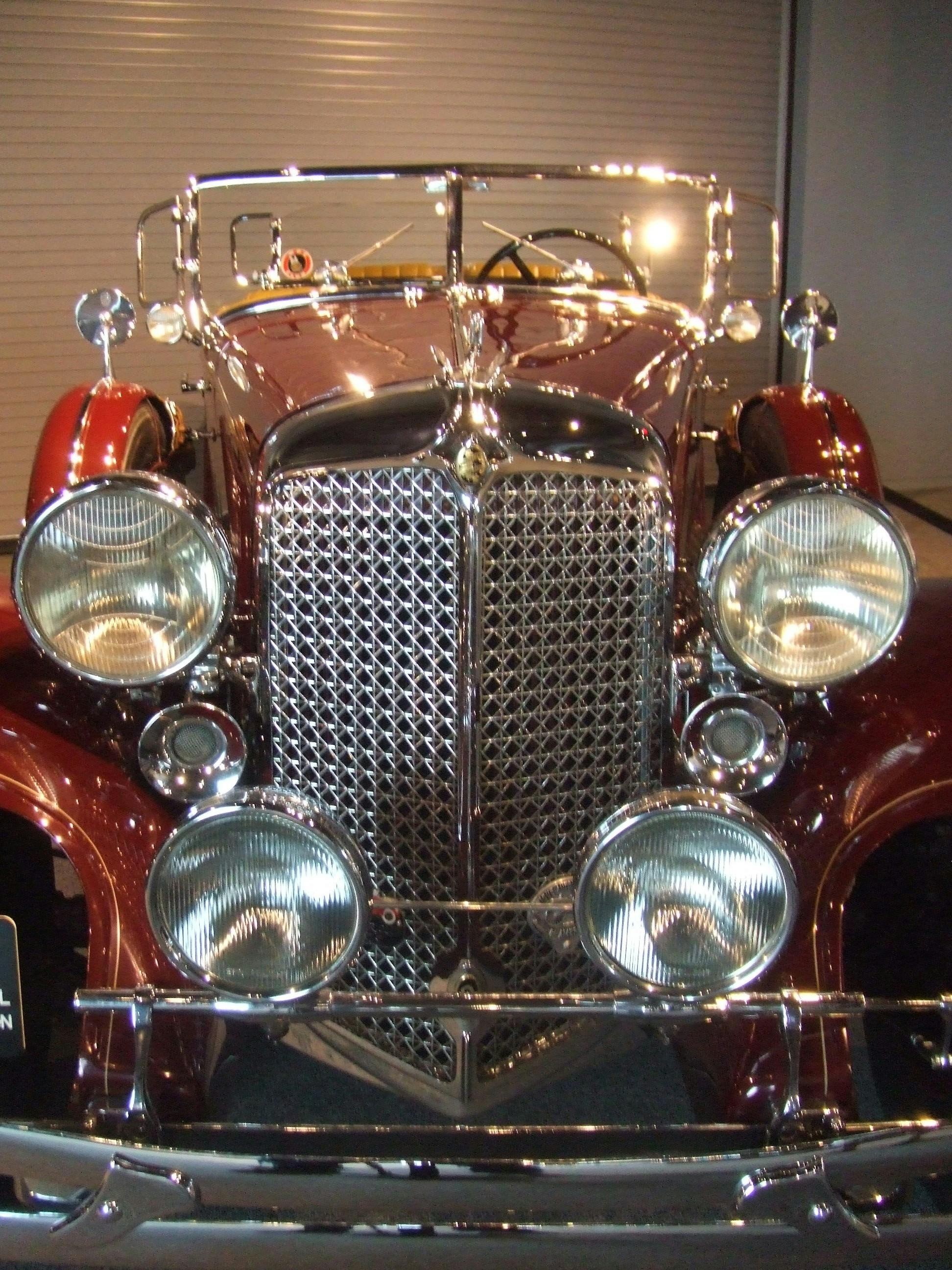 Μπροστινή όψη ενός vintage αυτοκινήτου με γυαλιστερή μάσκα, τέσσερις προβολείς και ένα ανακλαστικό καφέ σώμα.