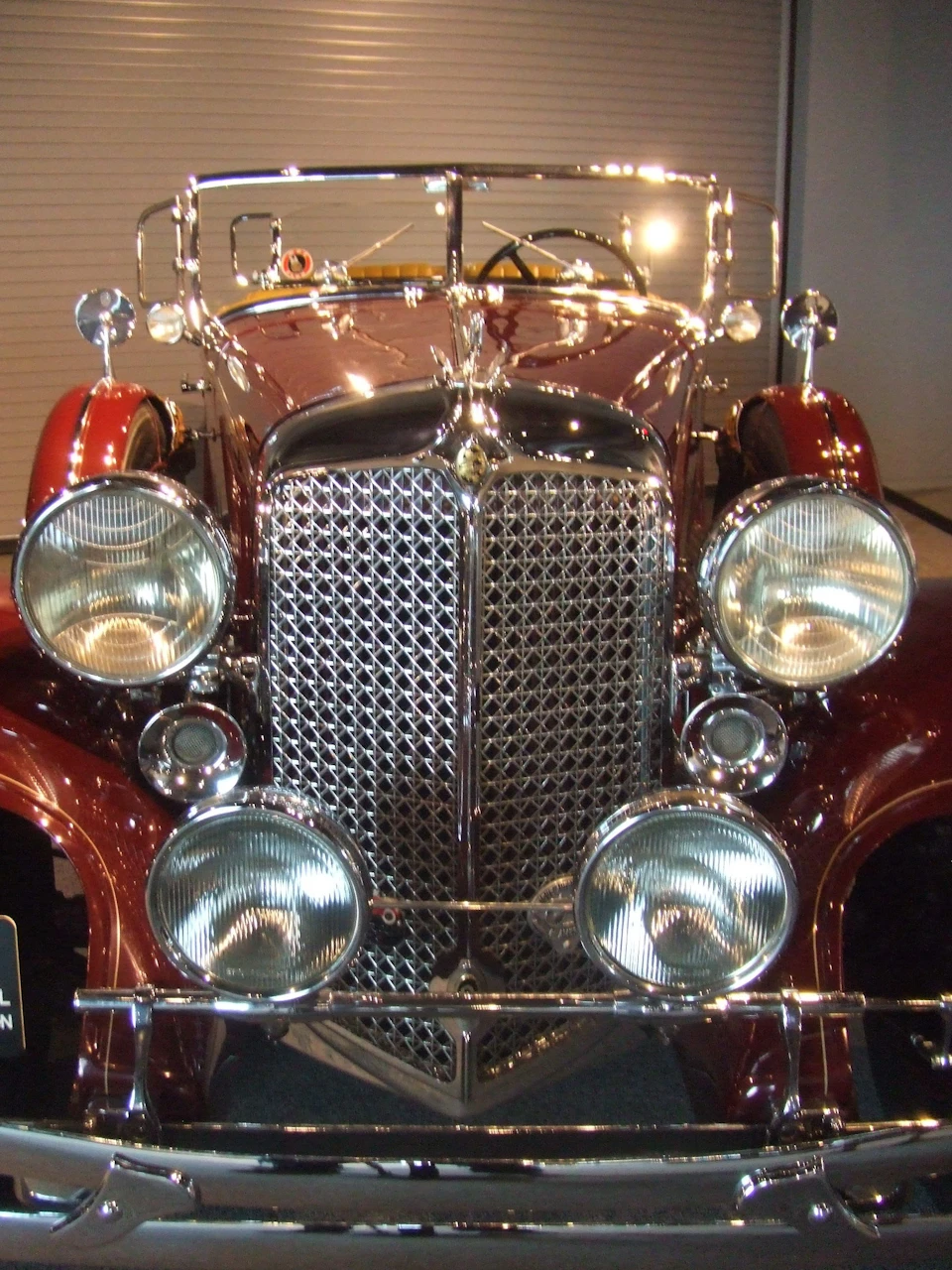Front view of a vintage car with a shiny grille, four headlights, and a reflective maroon body.