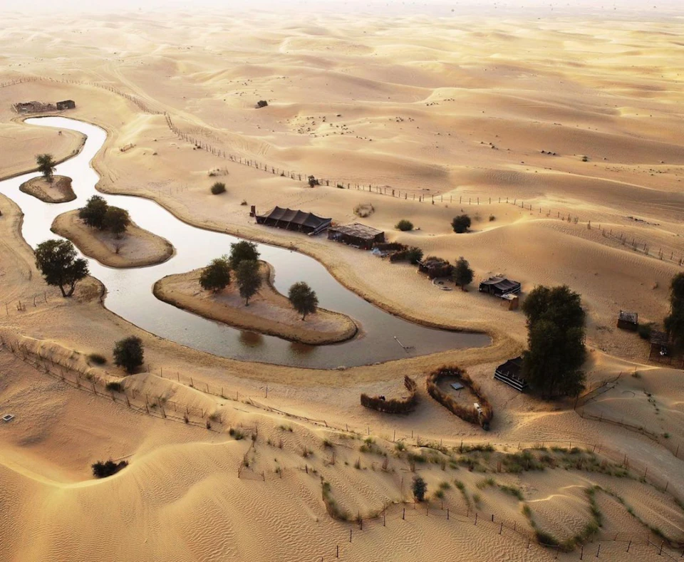 Aerial view of a desert oasis with scattered vegetation, small bodies of water, and several buildings.
